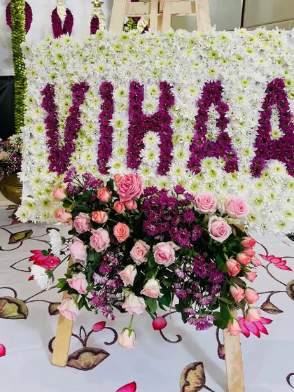 A personalized floral name board is a beautiful way to welcome a new baby. For Vihaa's naming ceremony, we crafted her name using deep purple chrysanthemums set against a bed of white flowers, with a fresh rose bouquet at the base.