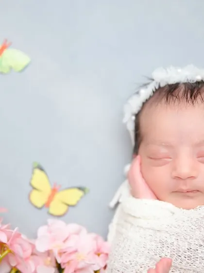 A close-up of a newborn's face, with her hand gently resting on her cheek. The soft lighting and simple wrap keep the focus on her pure innocence.