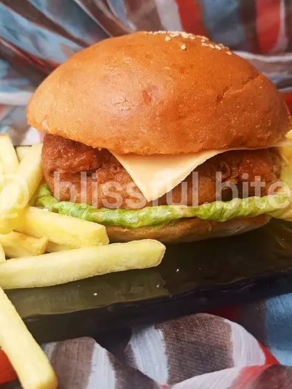 My bestselling Chicken Zinger Burger, featuring a crispy, juicy chicken fillet, fresh lettuce, and a slice of cheese in a soft, homemade bun, served with a side of golden french fries.