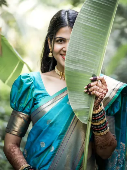 A playful and charming portrait of the bride peeking from behind a large banana leaf, with a bright smile.