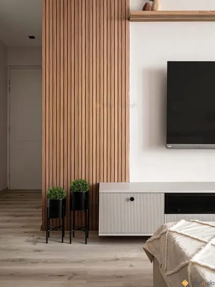 This bedroom TV unit is integrated into a wall of storage, with a vertical wood-slatted panel adding texture and visual interest. The two small plants bring a touch of nature indoors.