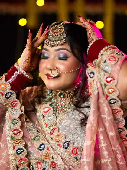 The bride adjusts her maang tikka, a candid-style shot that showcases the wearability and beauty of the makeup.