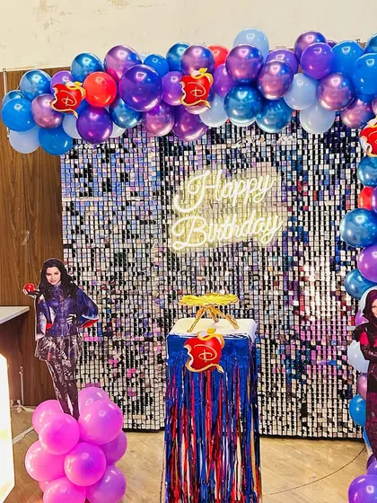 The main backdrop for the Descendants party, featuring a silver shimmer wall, character cutouts, and a marquee number '8'.
