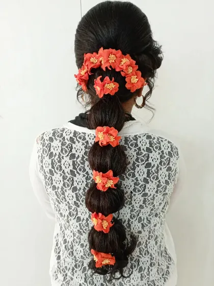 A traditional bubble braid hairstyle. I used orange floral accessories to add a festive touch, perfect for a family celebration or puja.