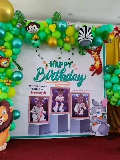 A vibrant jungle birthday backdrop with a balloon arch, large lion and rabbit cutouts, and a personalized banner with the birthday boy's photos.