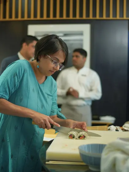 A participant carefully slices her sushi roll, a crucial step to ensure clean, beautiful pieces. This shows the focus and precision we teach in our classes.