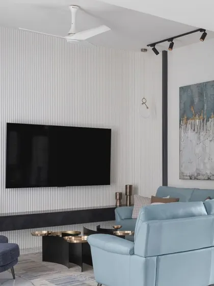 This view shows the full living area, with a textured TV wall panel providing a monotone backdrop. The layout seamlessly connects the living, dining, and kitchen spaces while allowing each to have its own distinct character.
