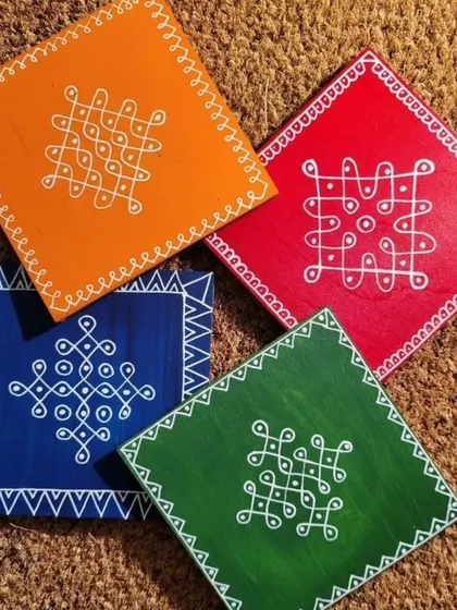 A set of four colorful coasters, each hand-painted with a unique Kolam pattern. These vibrant squares are perfect for protecting your surfaces while adding a pop of color and culture.