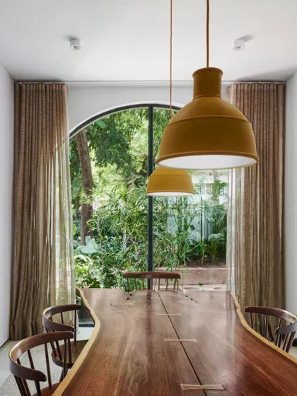 The dining table in our studio, framed by an arched French window that looks out onto lush greenery. This seamless integration of indoor and outdoor living is a principle we apply to our own workspace.