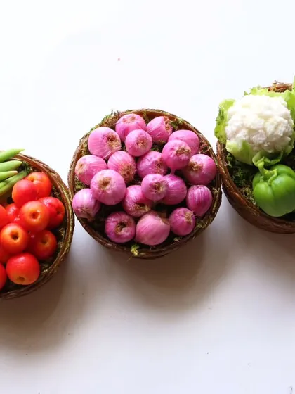 Three baskets of miniature vegetables: tomatoes and beans, onions, and cauliflower and capsicum.