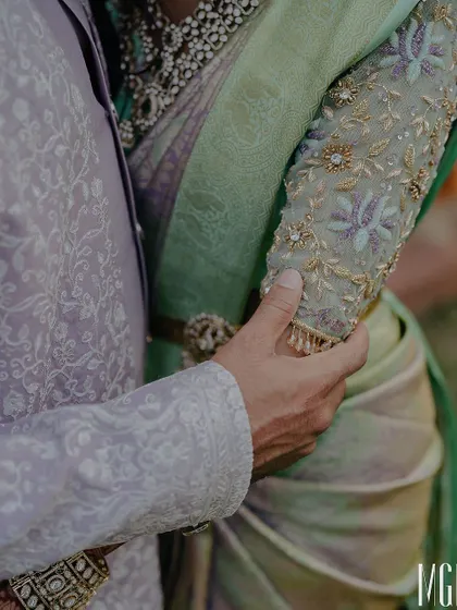 A detail shot focusing on the couple's hands and their exquisite traditional attire. This artistic close-up highlights the intricate embroidery and the gentle touch that speaks volumes.