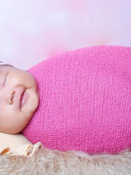A beautiful smiling baby girl, happily swaddled in a bright pink wrap. It's a joy to capture these happy expressions when babies are awake and content.