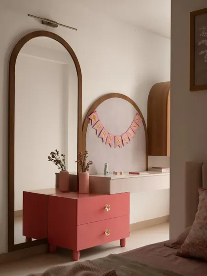 A custom vanity and dresser area designed for a young girl's room. The soft pink drawers and arched details create a delightful personal space, complemented by a full-length arched mirror.
