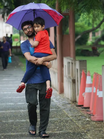 A father shields his son from the Delhi monsoon with an umbrella. This candid shot captures a simple, protective bond between family, a theme I often explore in my street portraiture.