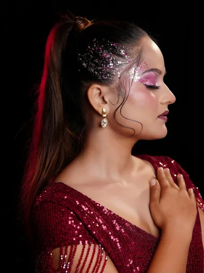 A side profile of a glamorous party look, highlighting the pink glitter eyeshadow and sleek high ponytail.