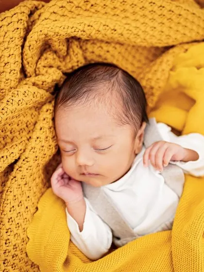 A newborn boy sleeping soundly in his own crib, wrapped in a cozy yellow blanket. These photos will be such a precious memory of his first room.
