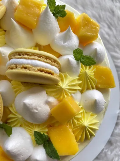 A close-up of the toppings on the mango cake, showing the fresh mint leaves, meringue, and macarons.