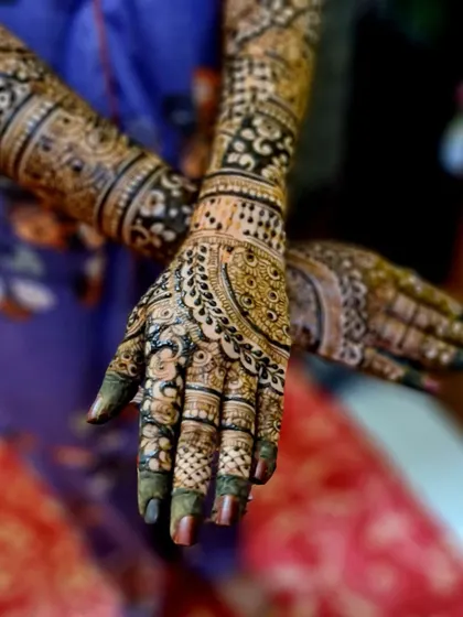A close-up of a bride's hands, highlighting the intricate finger details and the beautiful mandala design on the back of the hand.