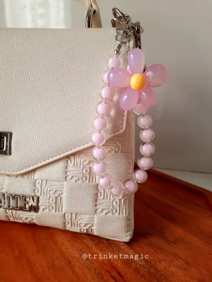A delicate, handmade pink beaded charm with a flower accent, shown here on a white handbag. It’s a perfect example of how my charms can elevate your everyday accessories.