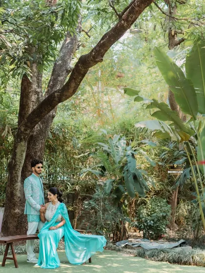 A serene moment captured in a beautiful garden setting. The way she sits while he stands beside her creates a lovely composition, showcasing their connection amidst the tranquility of nature.