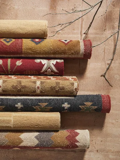 A stack of rolled-up rugs, showcasing a variety of colors and tribal-inspired patterns. This is a great way to display the breadth of a collection in a single, visually interesting shot.