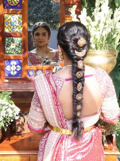 A beautiful shot capturing the bride looking in the mirror. It provides a perfect view of the intricate back design of her blouse and her traditional braided hairstyle.