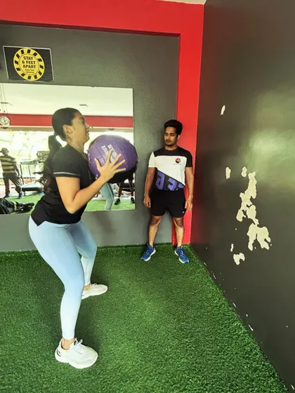 A coach watches as a client performs a medicine ball throw, providing feedback to improve her power and technique.