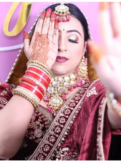 A creative bridal pose highlighting the intricate henna and the stunning polki jewellery set against the rich maroon velvet of the lehenga. The red bangles complete the traditional bridal look.