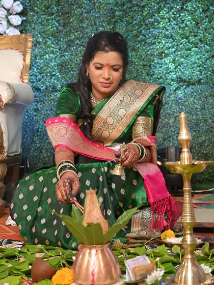 The bride participates in the engagement pooja. Her traditional look, from the makeup to the green Paithani saree, is perfect for the sacred rituals of the day.