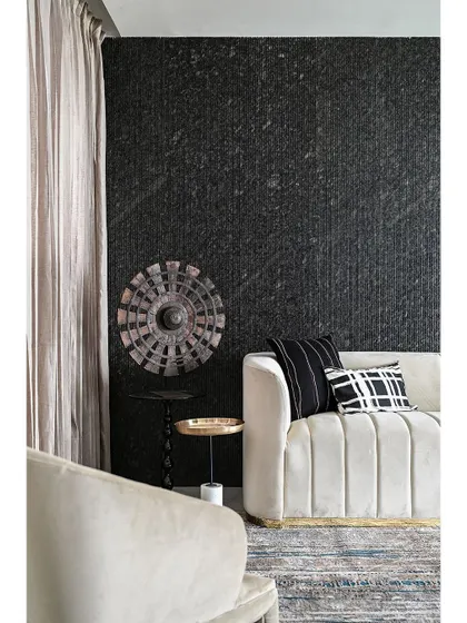 A close-up view of the textures and materials used in a lounge area. The channel-tufted sofa, patterned pillows, and the rough texture of the black stone wall demonstrate a commitment to quality craftsmanship and detail.