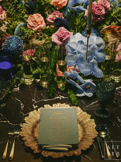 The dinner setting at 'Midnight Mirage'. Rich overlays, plush blue and pink blooms, and soft gold accents on a marble tabletop created a tablescape that exuded beauty and wonder.