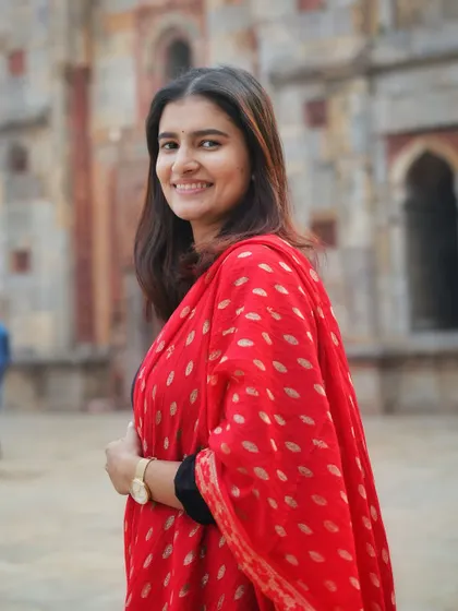 A bright, smiling portrait that perfectly captures her personality. The combination of the simple black kurta and the ornate red dupatta is a classic ethnic look.