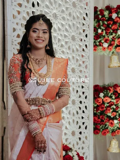 A happy smile from one of my beautiful brides. She is glowing in a custom-fit blouse with delicate floral embroidery on sheer sleeves, perfectly complementing her off-white and orange Kanchipuram saree for her wedding day.
