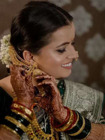 A close-up of the bride getting ready, putting on her traditional gold earrings, with beautiful henna on her hands.