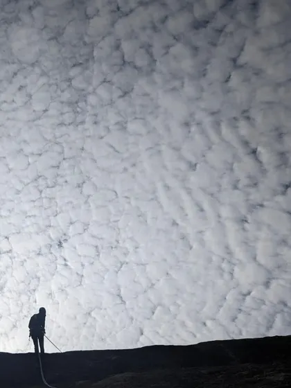 A dramatic silhouette of a climber rappelling against a mackerel sky at Hosadurga. Route development days are often filled with stunning natural beauty.