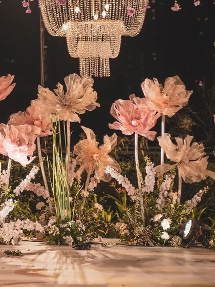 A full view of the stage area, where oversized paper flowers seem to grow from a garden of white blooms. The design feels both organic and fantastical, perfect for a modern fairytale wedding.