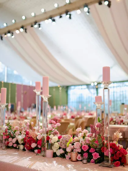 The head table at the pastel reception, featuring a lush runner of pink and white flowers and tall, elegant glass candle holders.