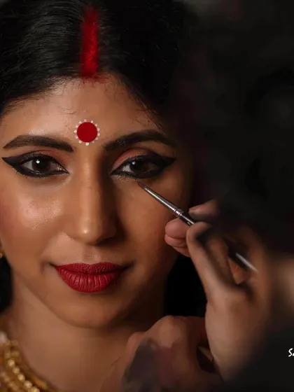A detailed shot of the final 'aharya' or adornment. The application of makeup and jewelry completes the transformation from a clay figure to the revered image of the Goddess.