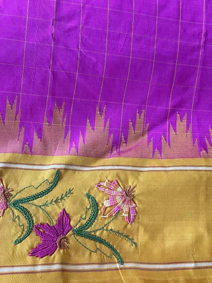 The border of this vibrant Kanjeevaram silk saree is adorned with Kamal Kadai embroidery. This stitch, known for its woven floral effect, brings a unique texture and dimension to the pure silk, blending tradition with luxurious color.