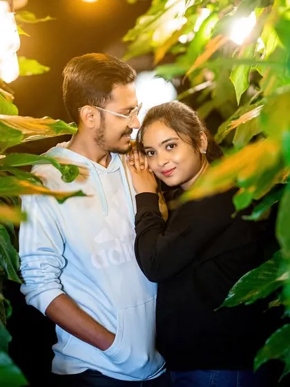 An intimate night portrait, with the couple framed by leaves and soft lighting.