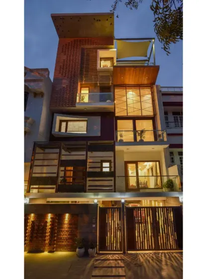The Kavyam Residence, built on a compact 168 sqm plot, fuses contemporary design with traditional Indian elements. The façade at night reveals a complex interplay of light, texture, and materials, including brick jaali, wood, and a tensile roof.
