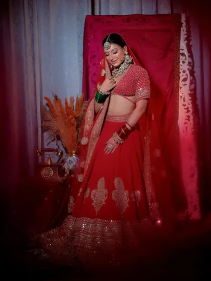 A full-length portrait of a bride in a simple yet elegant red lehenga. The soft, diffused lighting and vignette effect create a dreamy, romantic mood.