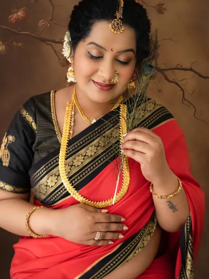 A close-up shot focusing on the serene expression of a mom-to-be in a traditional saree, holding a peacock feather, a symbol of beauty and grace.