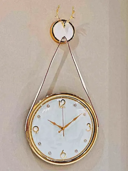 This unique hanging-style wall clock offers a fresh take on timekeeping. The white and gold clock face is suspended from a decorative mount, creating a light and elegant look that feels both modern and timeless.