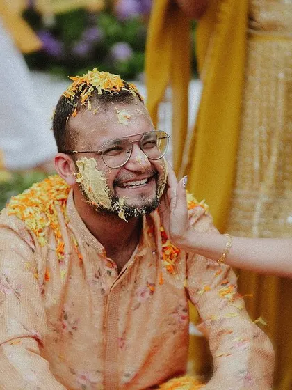 A tender moment as a guest affectionately applies haldi to the groom's cheek.