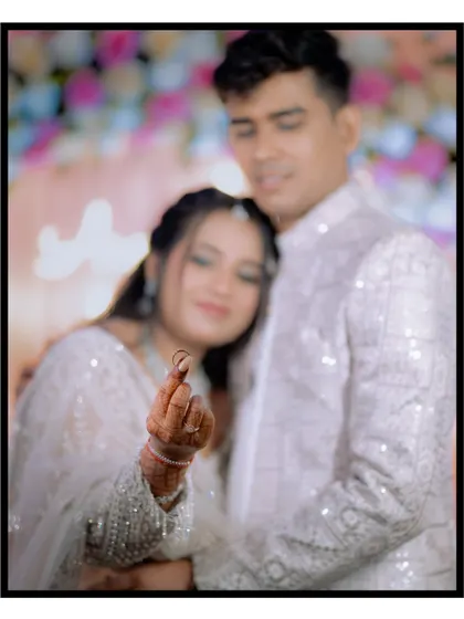 A creative portrait where the bride proudly displays her new ring to the camera. The focus is sharp on the ring, with the happy couple softly blurred in the background.