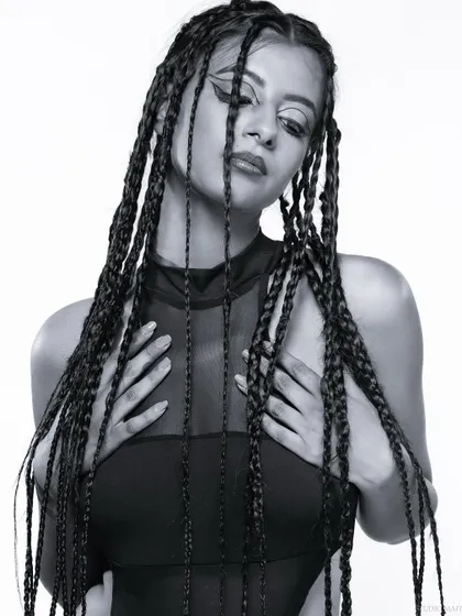 A black and white portrait of a model with braids, her hands framing her face.