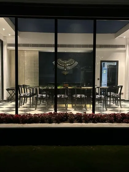 The winter dining pavilion viewed from the lawn at night. The interior lighting creates a warm, inviting glow, turning the structure into a beautiful lantern in the garden.