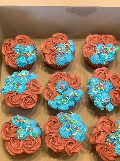 A fun and colorful cupcake set. Each cupcake is decorated with a mix of brown buttercream rosettes and bright blue piped stars, topped with rainbow sprinkles for a festive look.