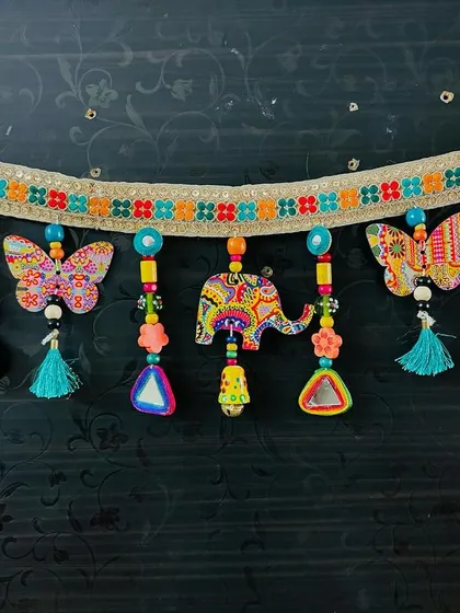 The 'Bageecha' Toran hanging against a dark background, making the vibrant colors of the art prints and tassels really stand out.